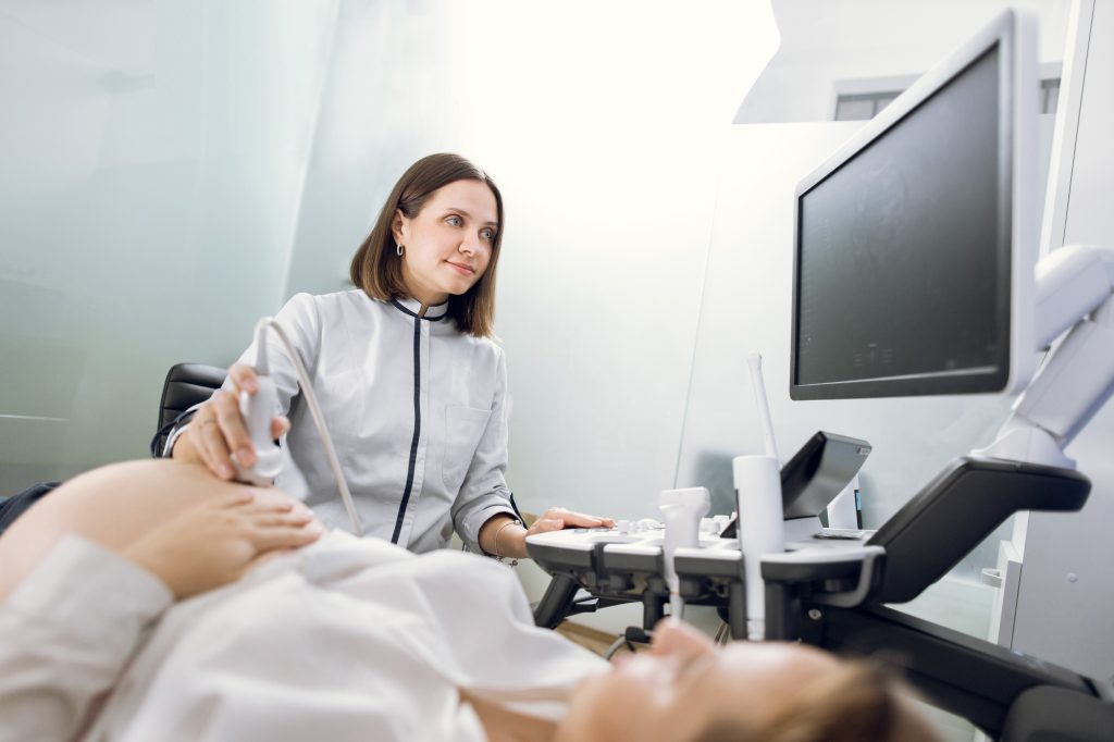 Young smiling professional attractive woman doctor doing 3d ultrasound on belly